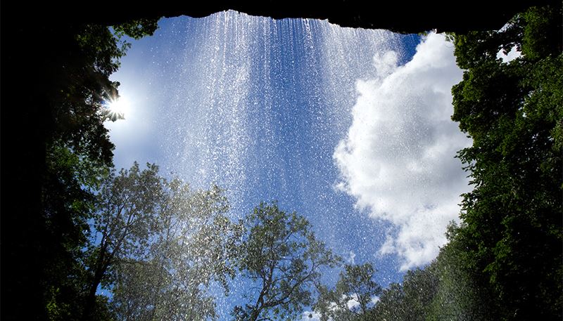 From the perspective of looking out from a cave, you see a thin waterfall